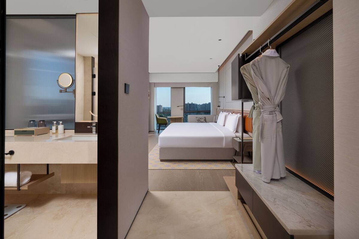 Habitació d'hotel moderna amb un llit gran, zona de seients amb vistes, bany amb mirall i una bata penjada a la porta.