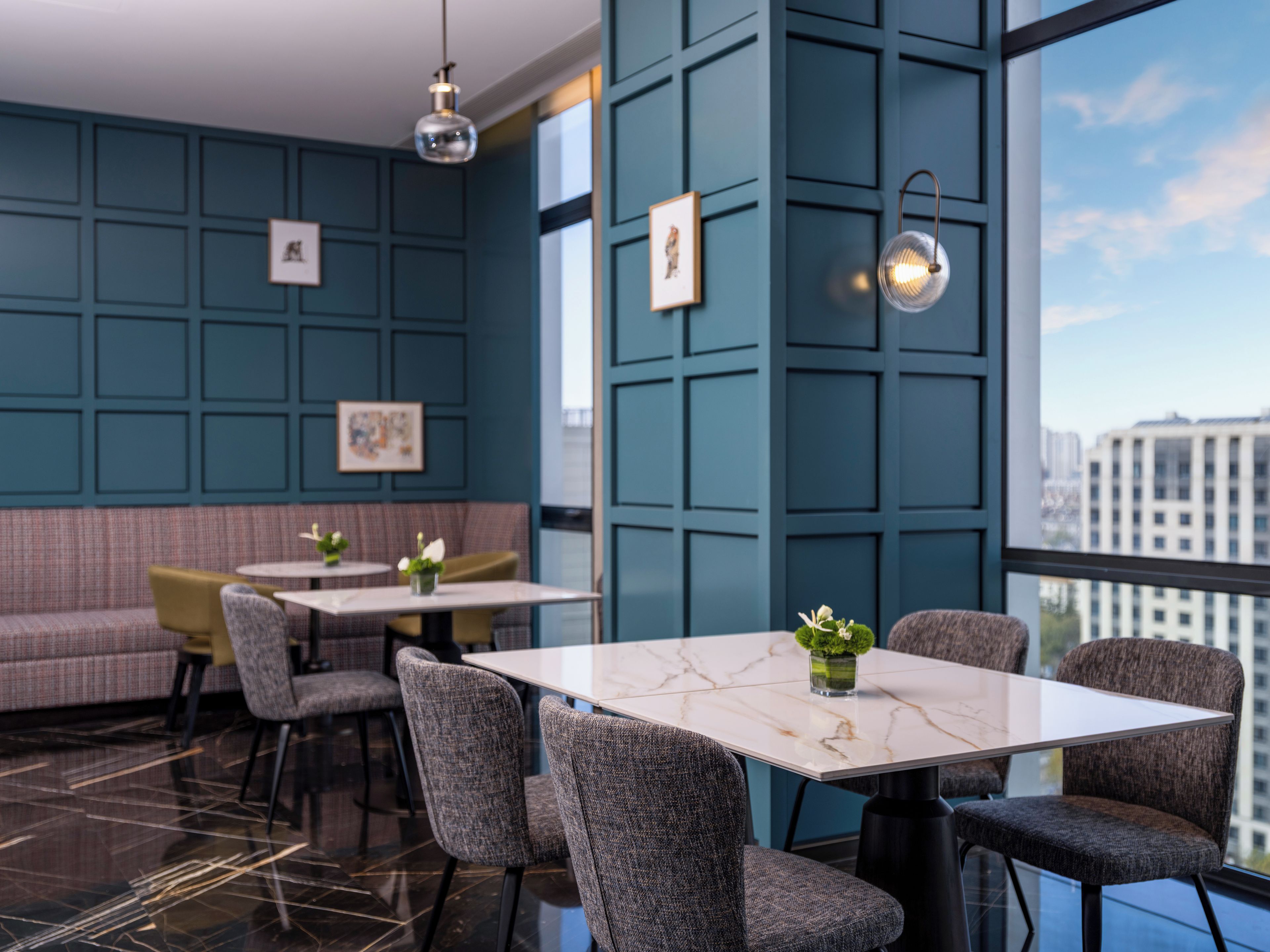 Un interior moderno con una mesa de mármol, sillas tapizadas en gris, paredes con paneles en color verde aguamarina y obras de arte enmarcadas.
