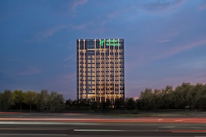 A tall hotel building with a modern design, featuring a prominent logo at the top. - Holiday Inn Beijing Daxing Centre By Ihg (Daxing)