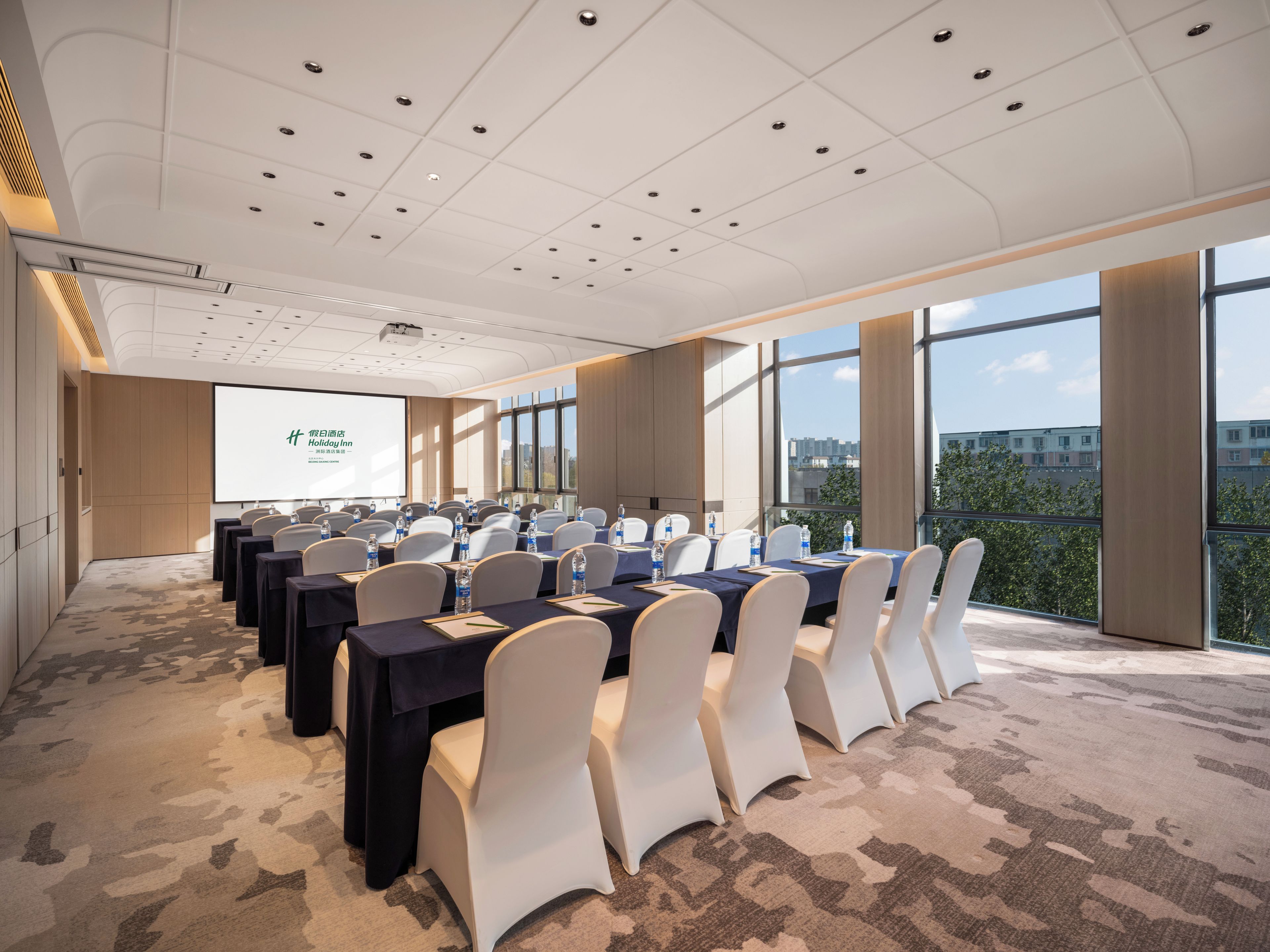 Un salón de conferencias con una pantalla grande, varias mesas y sillas.