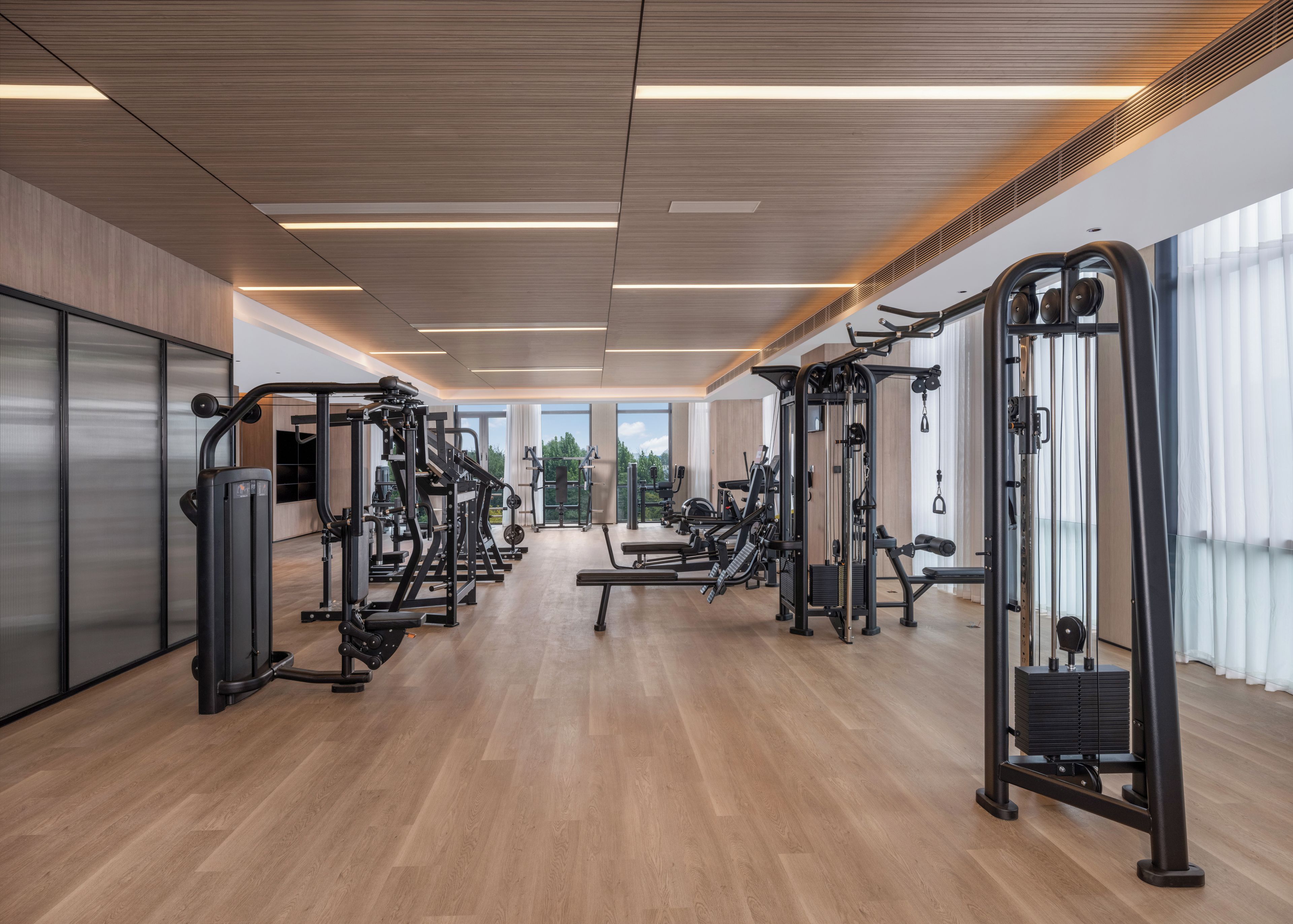 Una palestra moderna con diverse macchine per esercizi, ampie finestre e pavimento in legno.