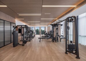 Un gimnasio moderno con diversas máquinas de ejercicio, amplias ventanas y suelo de madera.