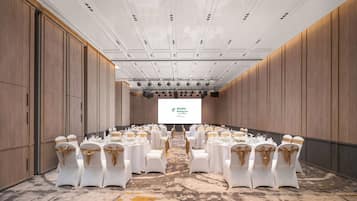 A conference room with white tables and chairs, a large screen at the front, and wooden paneling on the walls.