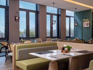A modern dining area with high windows, green upholstered seating, and a wooden table with cutlery. - Holiday Inn Beijing Daxing Centre By Ihg (Daxing)