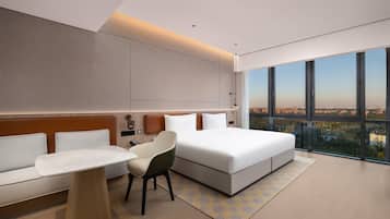 Una habitación de hotel moderna con una cama grande, un sofá, una silla y un escritorio. Una ventana amplia ofrece vistas a la ciudad.