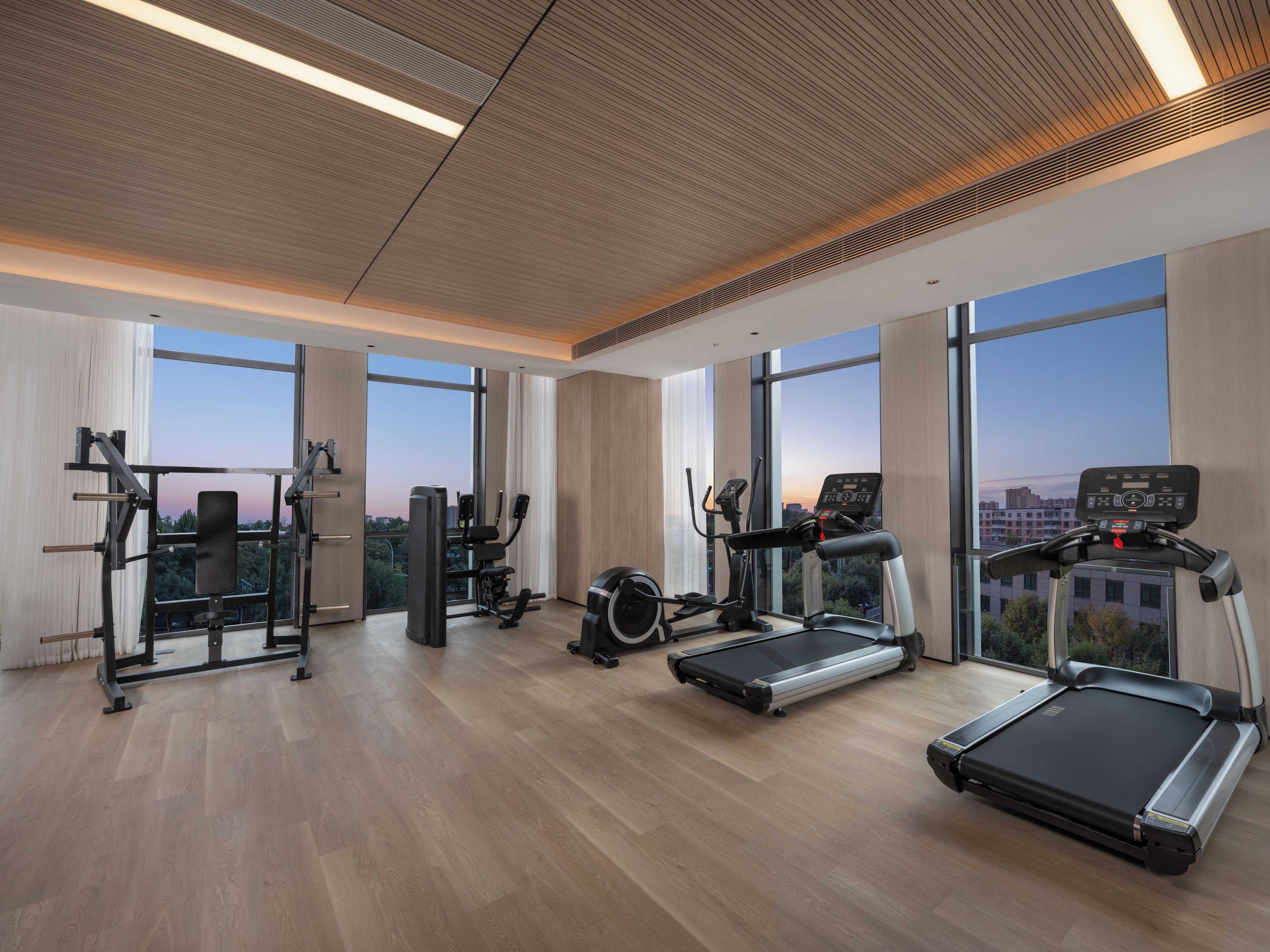 Un gimnasio moderno con diverso equipo de ejercicio, ventanas amplias y techo de madera.