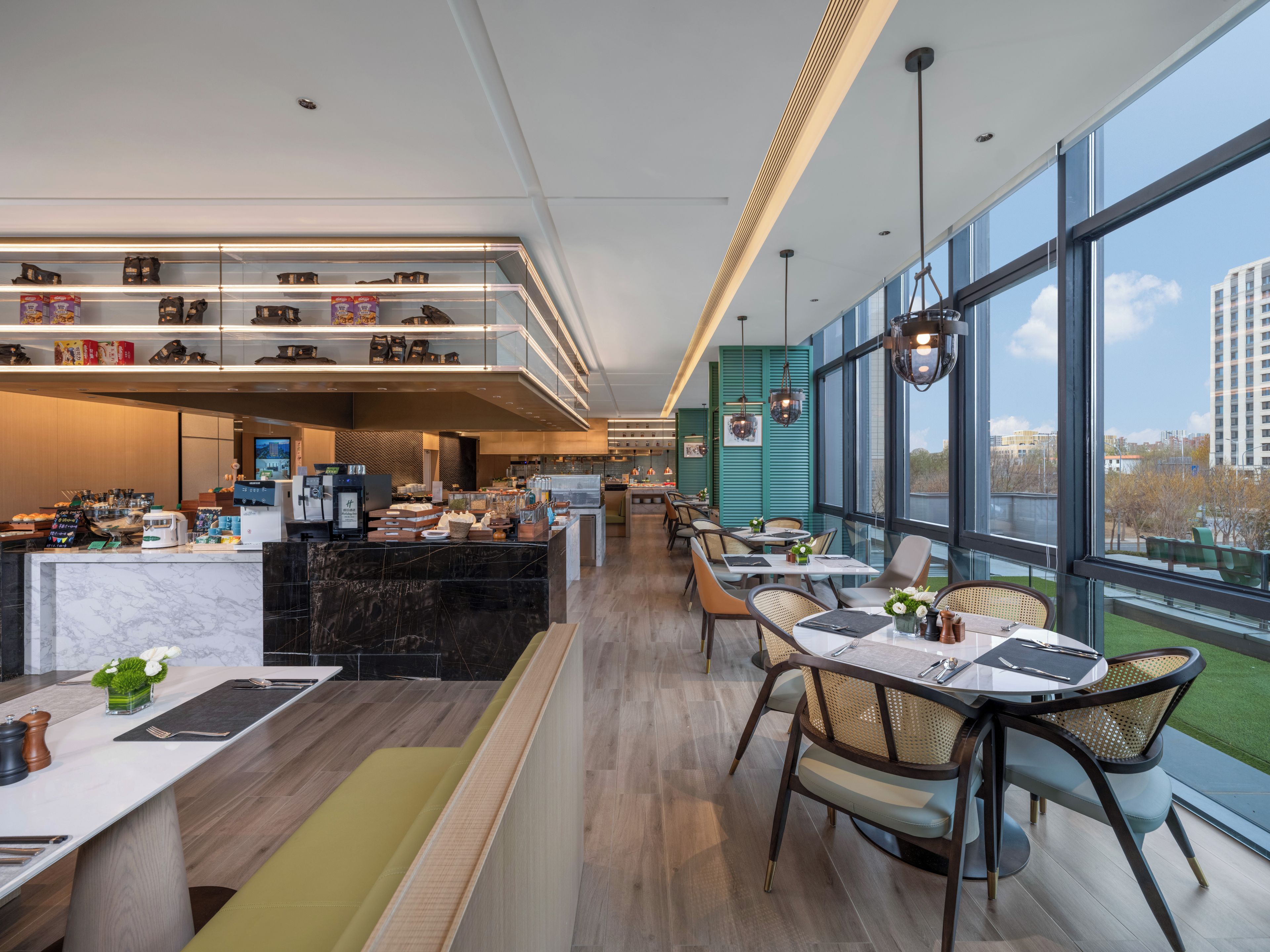 A modern restaurant with a long counter, seating area, and large windows offering views of the city.