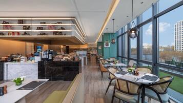 A modern restaurant with a long counter, seating area, and large windows offering views of the city.