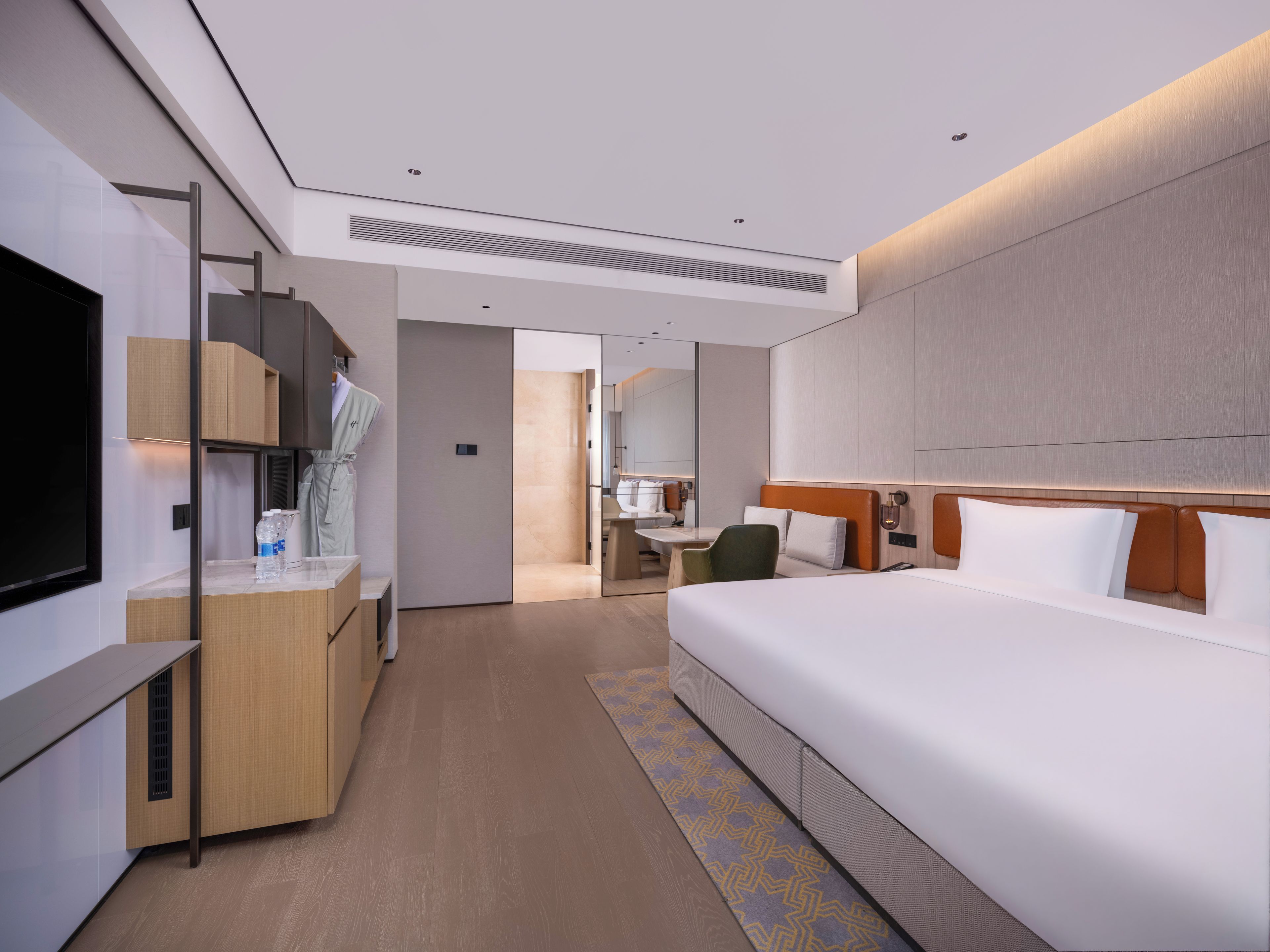 A modern hotel room with a large bed, a desk, a chair, and a television.