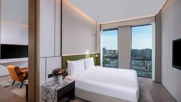 A modern hotel room with a large bed, a desk with a lamp, a chair, a TV, and a city view.