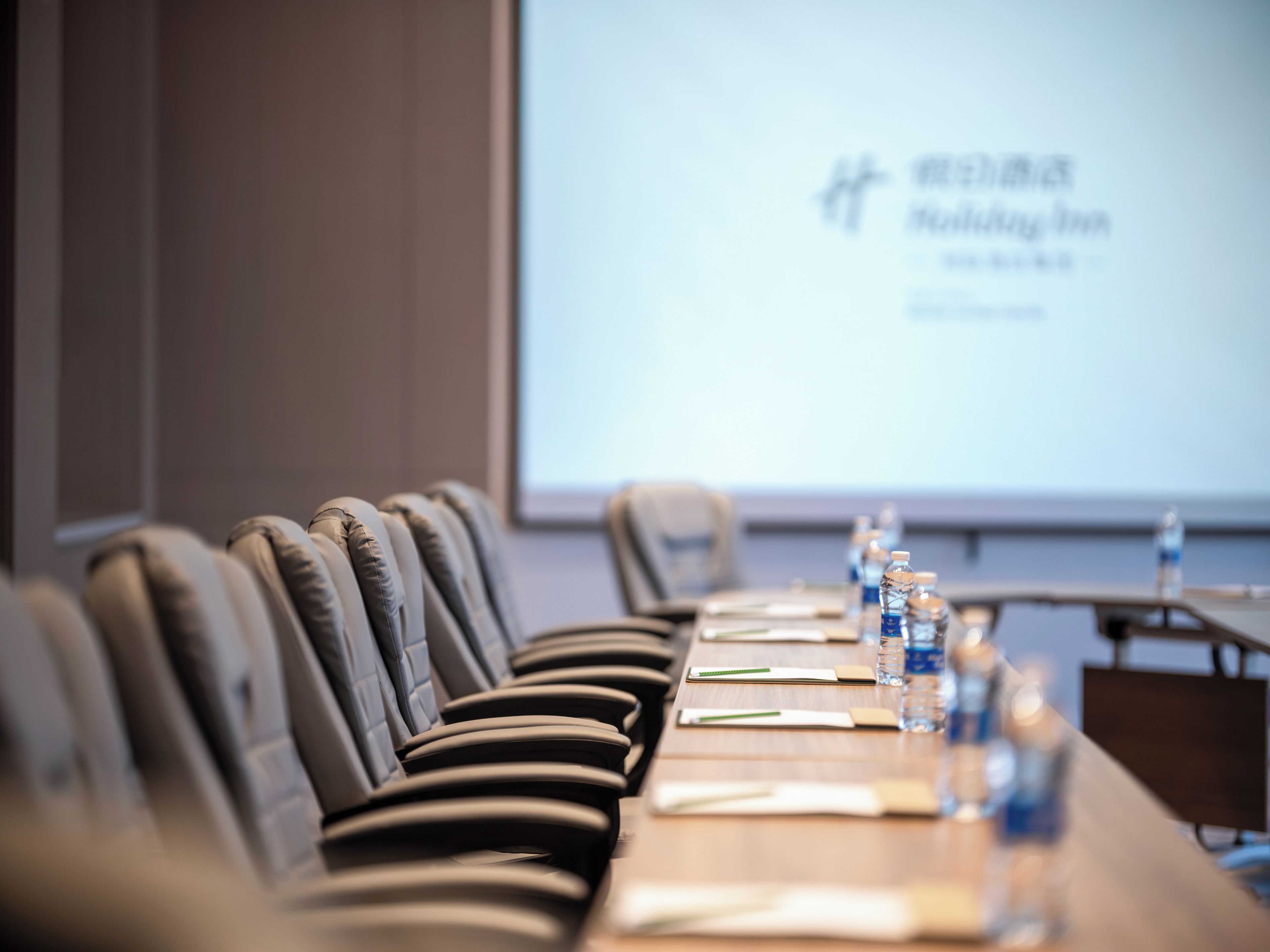 A conference room with a long table, chairs, water bottles, and a presentation screen.