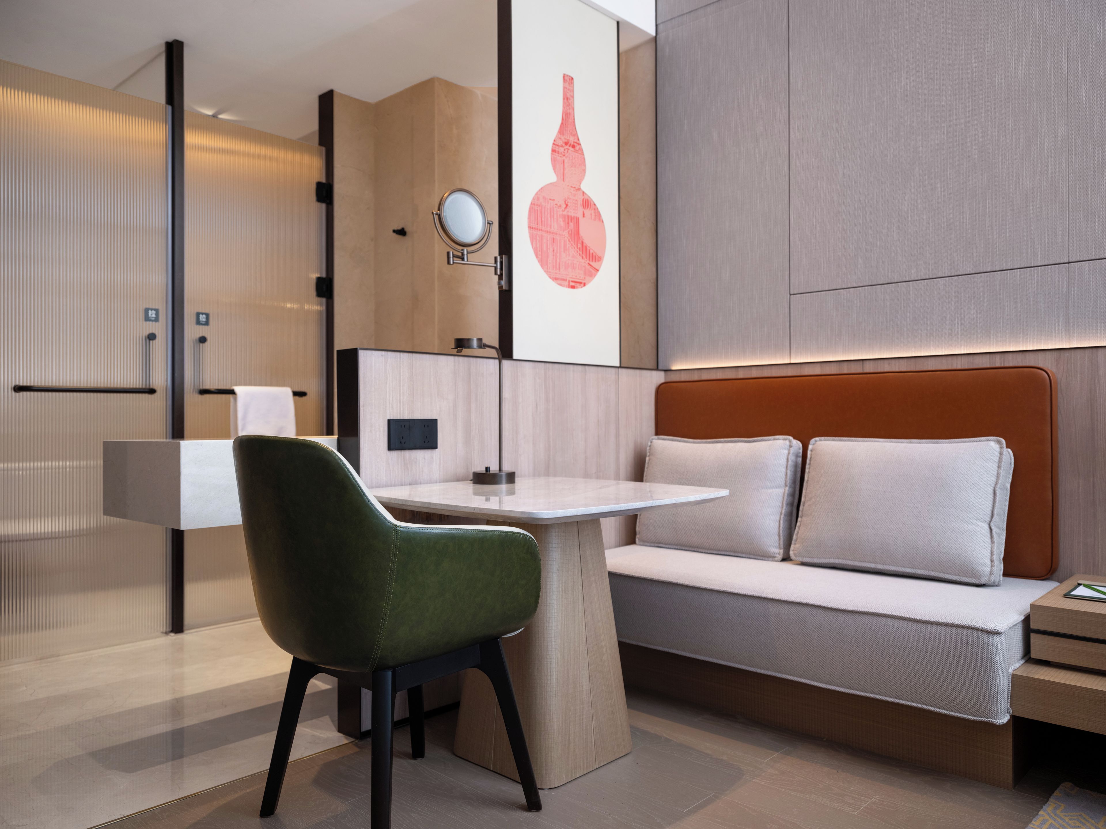 A modern hotel room with a green chair, a white sofa, a round mirror, and a wall-mounted artwork.