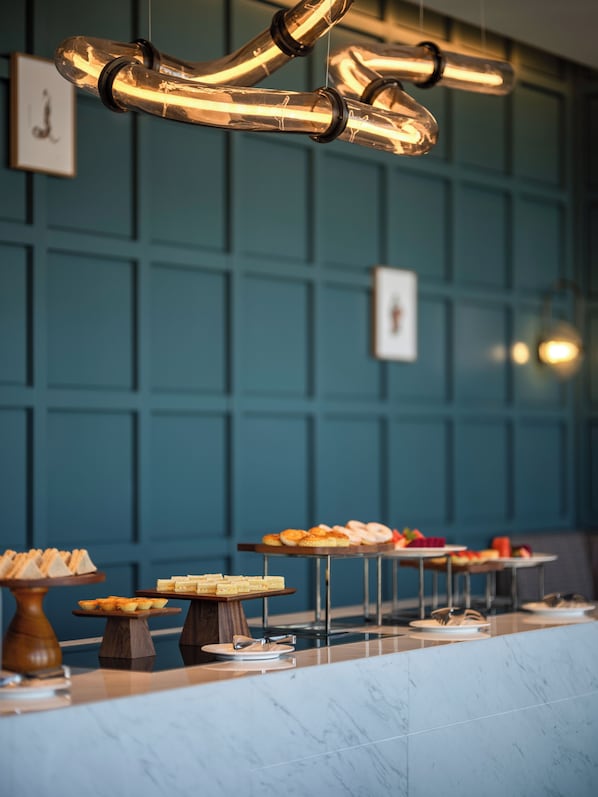 A buffet setup with various food items on wooden and metal serving boards, set against a teal wall with framed pictures. - Holiday Inn Beijing Daxing Centre By Ihg (Daxing)