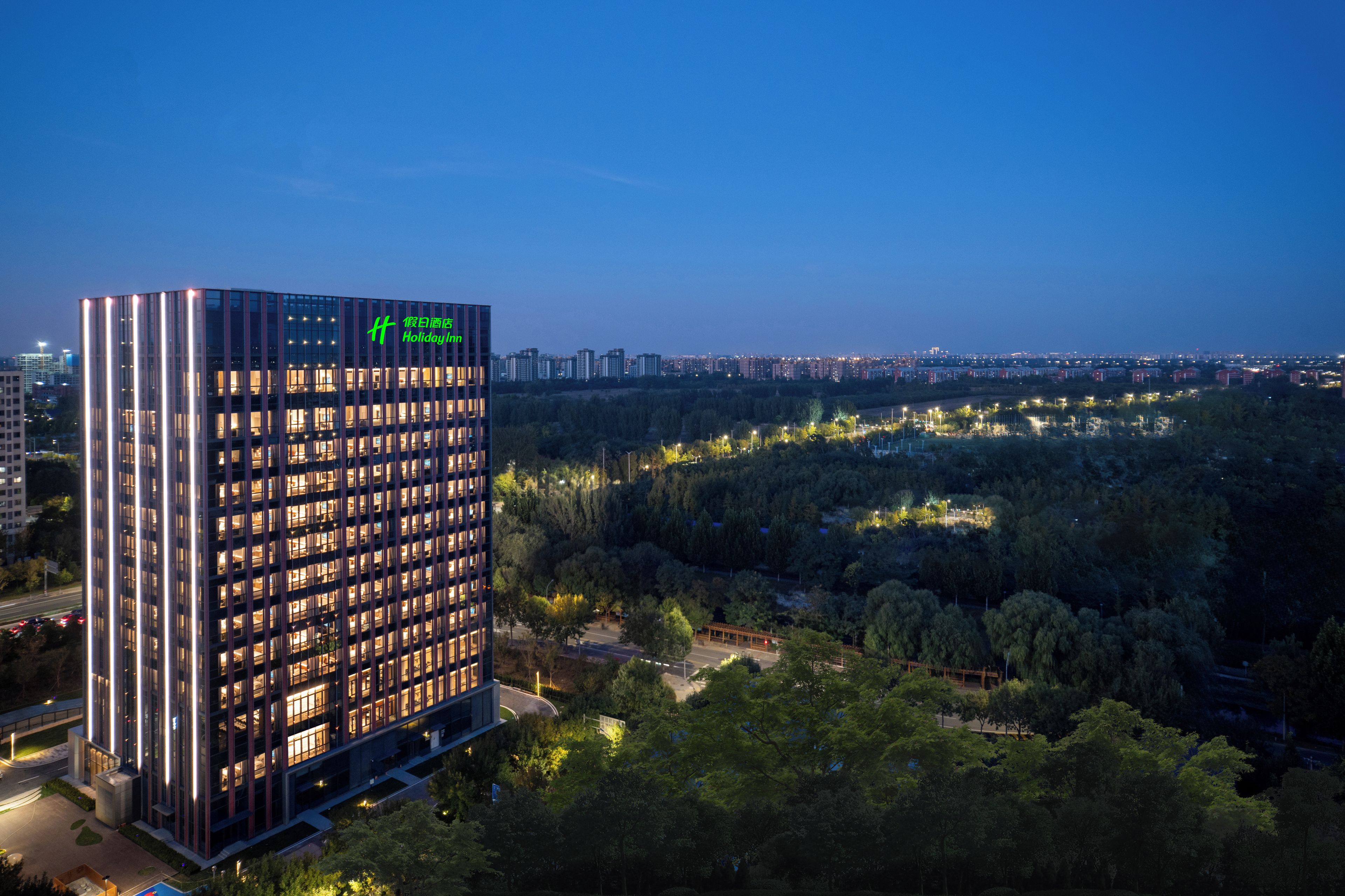 Moderni korkea hotellirakennus, jossa on useita kerroksia, suuret ikkunat ja huomiota herättävä vihreä logo ylimmässä kerroksessa.