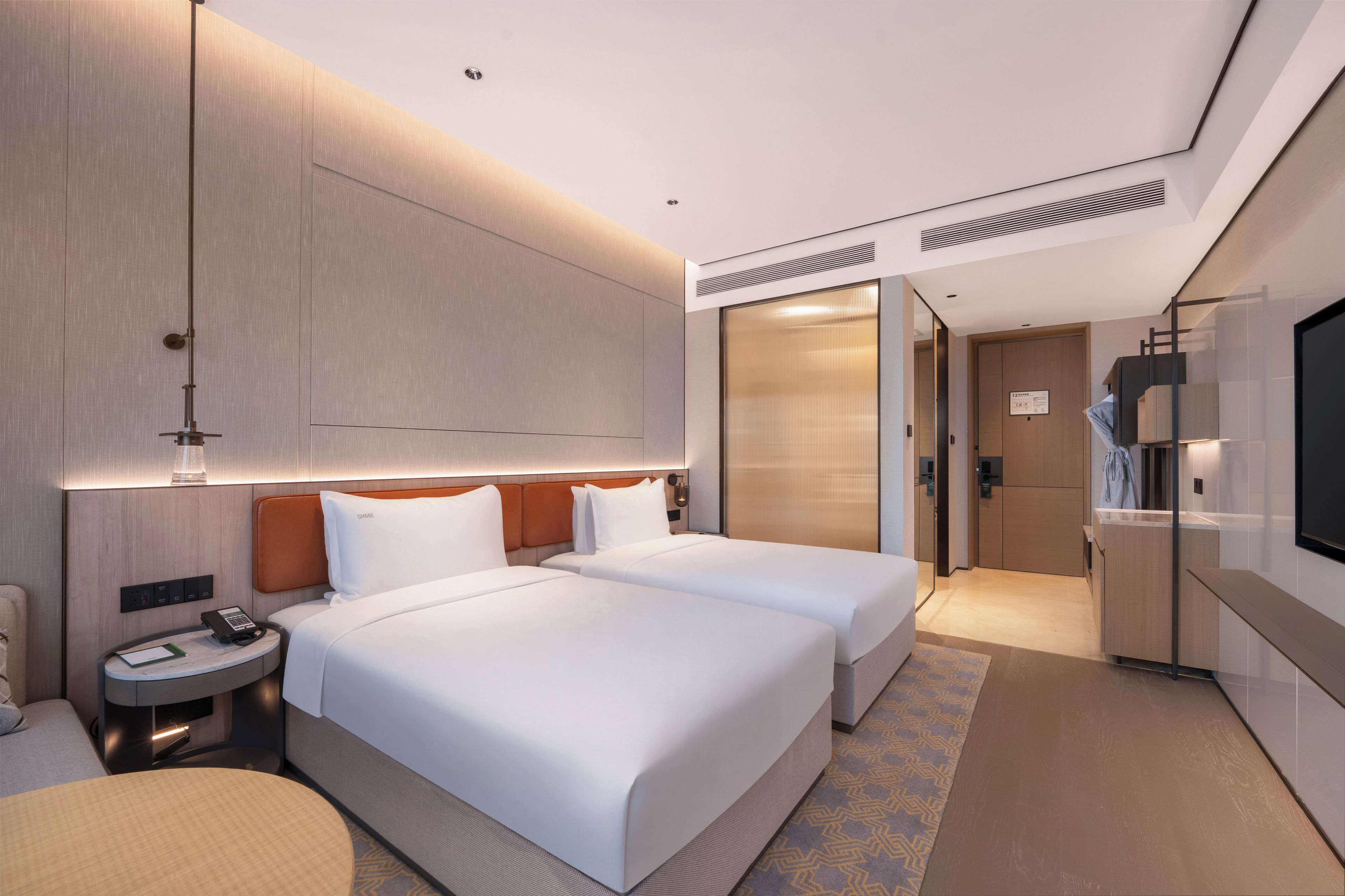 A hotel room with two beds, a desk, a chair, a TV, and a bathroom.