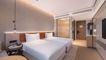 A hotel room with two beds, a desk, a chair, a TV, and a bathroom.