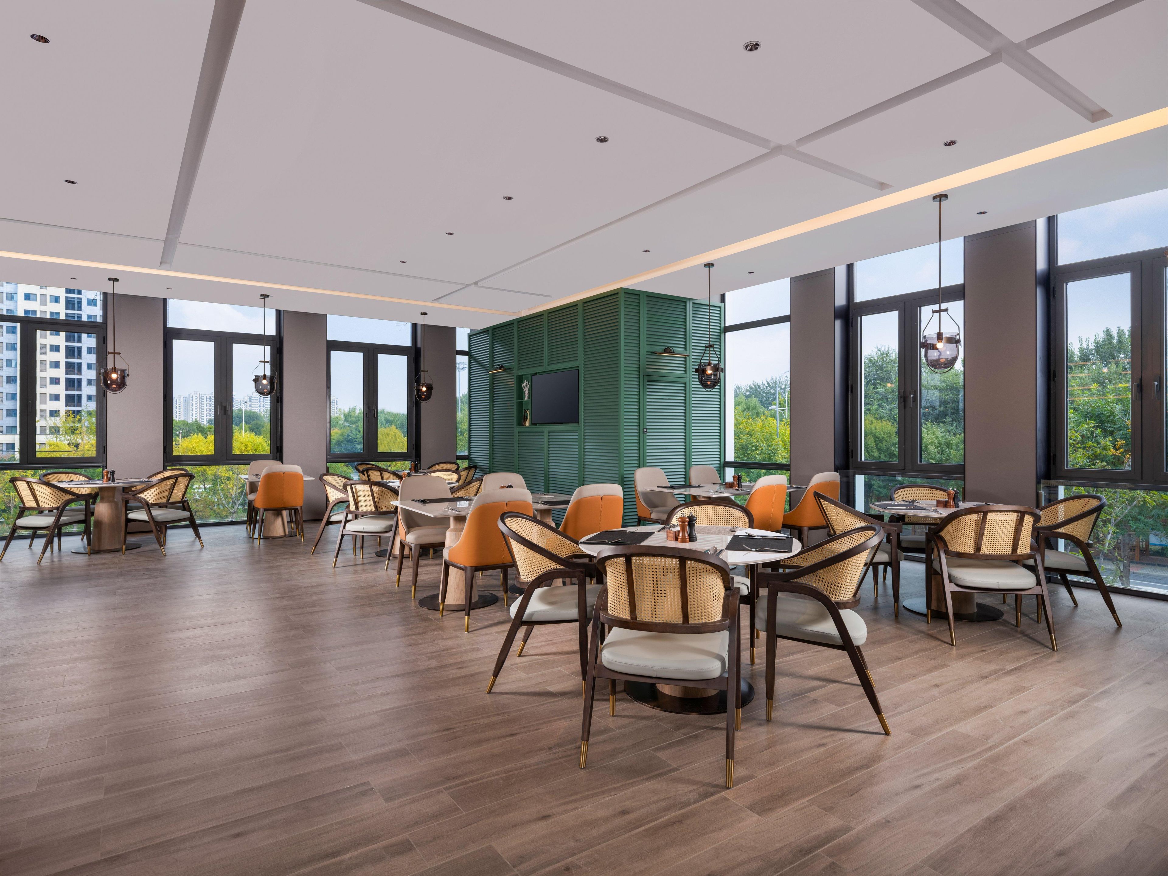A modern dining area with high ceilings, large windows, and a green accent wall.