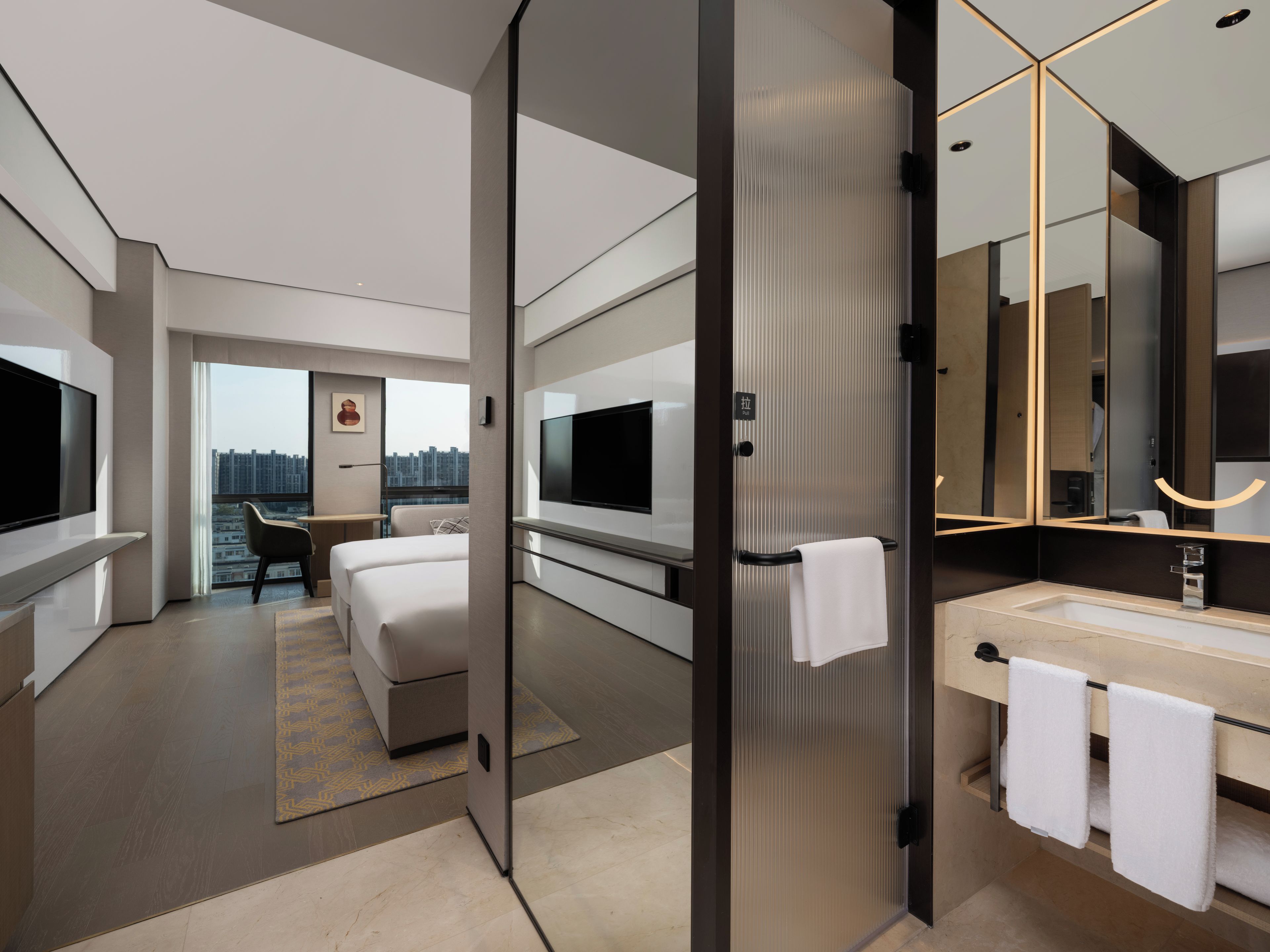 Una moderna camera d'hotel con un grande letto, una TV, un bagno con specchio e vista sulla città.