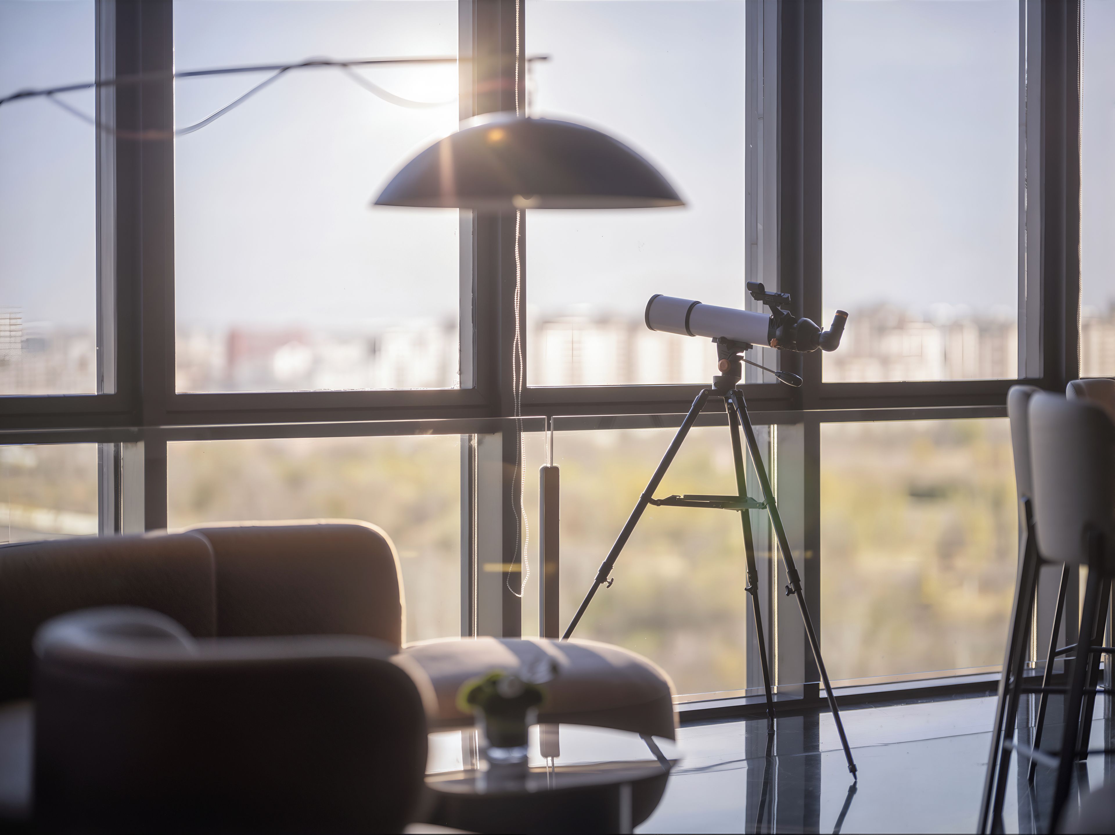 A room with a telescope on a tripod, large windows, a lamp, and a chair.