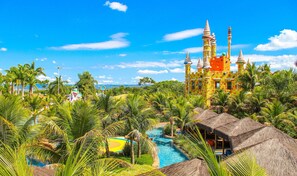 Un complexe hôtelier doté d’une structure colorée rappelant un château, d’une piscine et d’une végétation tropicale luxuriante.