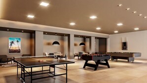 Un área recreativa moderna en el interior, con mesa de futbolín, mesa de ping pong y mesa de billar.
