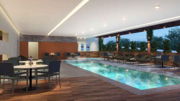 Un área interior de piscina moderna con suelo de madera, sillones reclinables y un comedor con mesas y sillas.