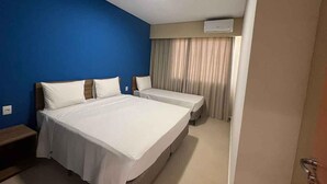 Habitación de hotel con una cama grande, otra más pequeña, un escritorio y una ventana con cortinas.