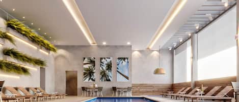Un área de piscina interior moderna con sillones de descanso, una mesa e iluminación empotrada en el techo.