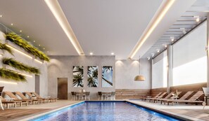 Un espace piscine intérieur moderne, doté de chaises longues, d’une table et d’un plafond pourvu d’un éclairage encastré.