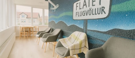 A waiting area with a mural, grey chairs, a table, and a sign that reads "FLATEY FLUGVÖLLUR".