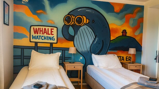 Ein Hotelzimmer mit zwei Betten, einem Wandgemälde eines Wals und einem Schild mit der Aufschrift 'Whale Watching'.
