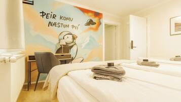 A hotel room with a bed, a desk, a chair, and a wall with a painting.