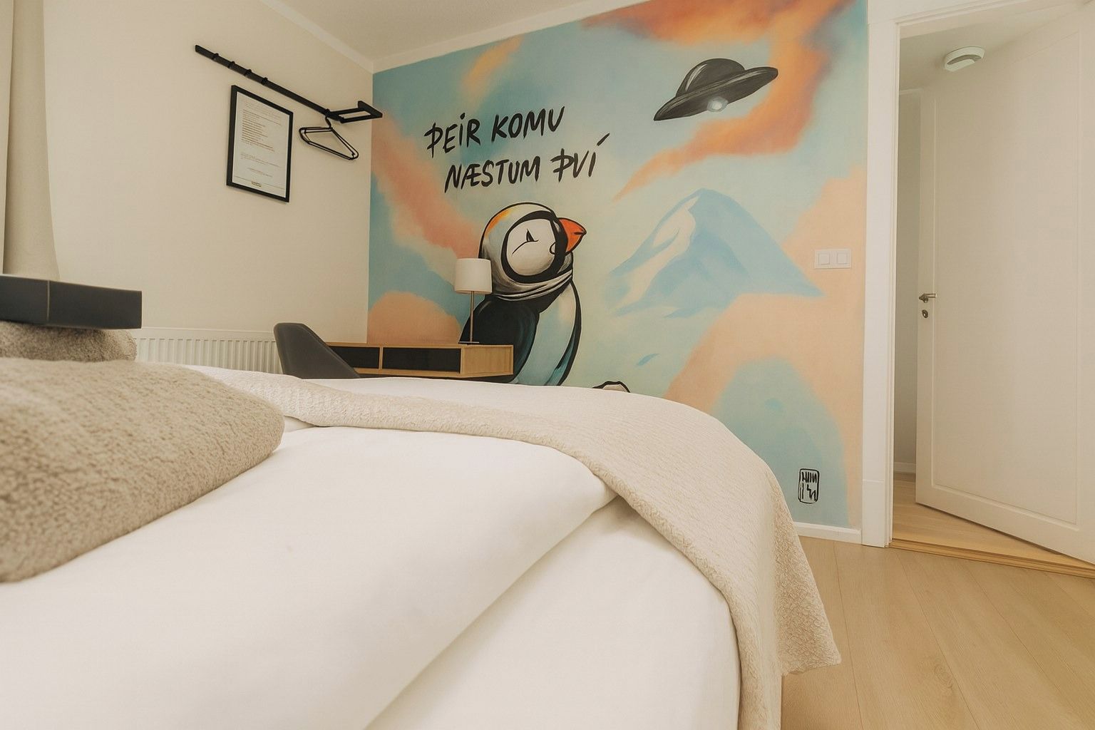A bedroom with a bed, a desk, and a wall with a colorful mural.