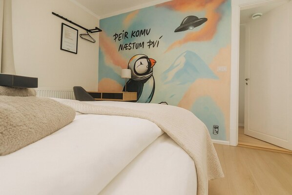 A bedroom with a bed, a desk, and a wall with a colorful mural. - Stykkisholmur Inn (Stykkisholmur)