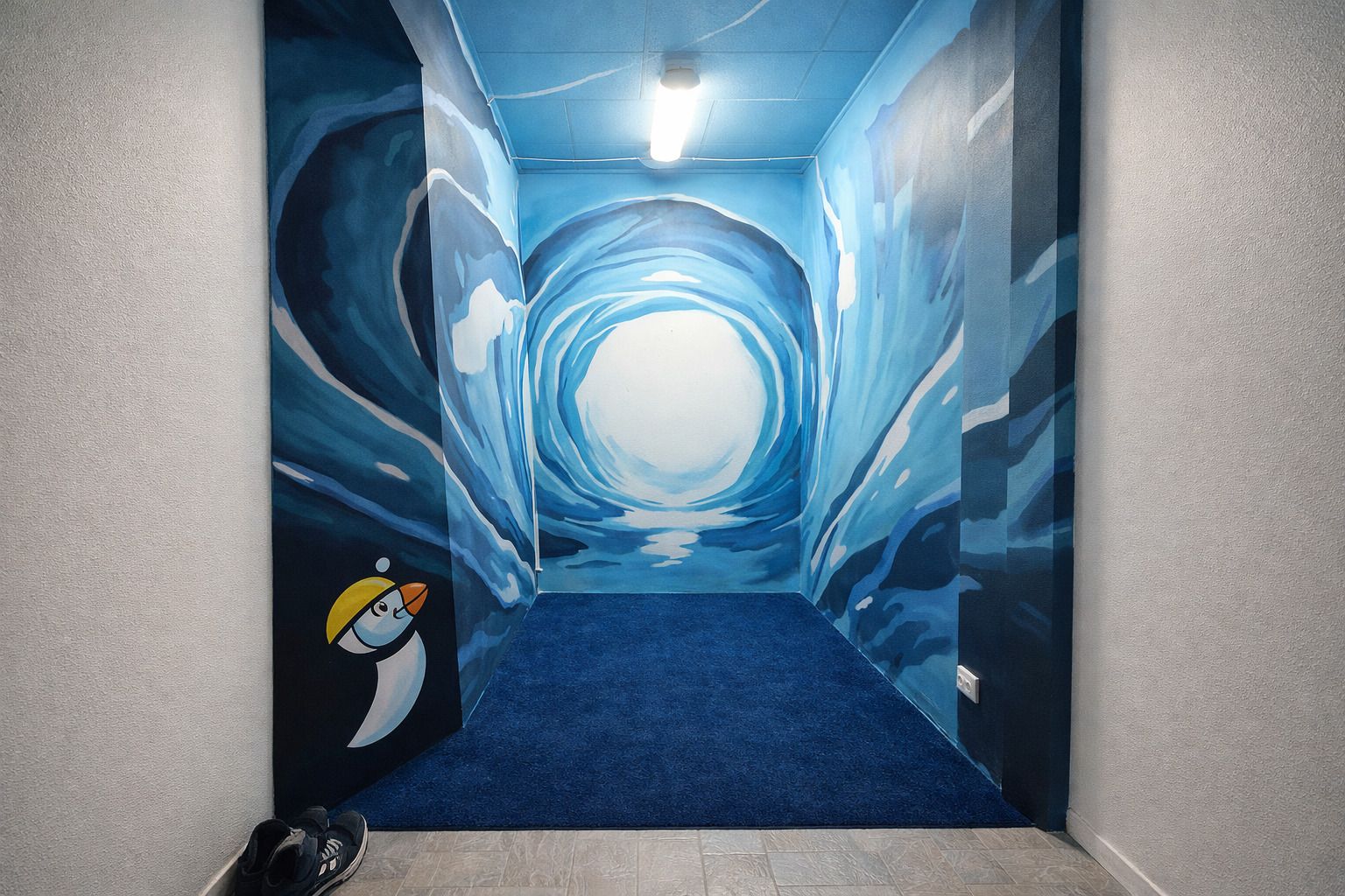 Un pasillo con alfombra azul y un mural de un túnel con un personaje de pingüino.