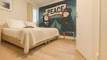 Una camera da letto con un letto, un comodino, un affresco raffigurante due pinguini e una finestra con tende.