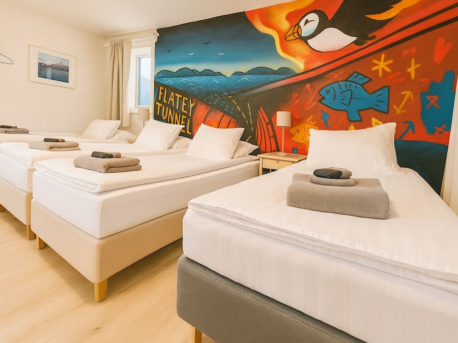 A hotel room with three single beds, each with a pillow and a rolled towel. The room has a large window with a view of the sea and a colorful mural on the wall.