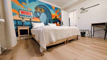 Quarto com cama, mesa de cabeceira, escrivaninha e parede com um mural colorido.