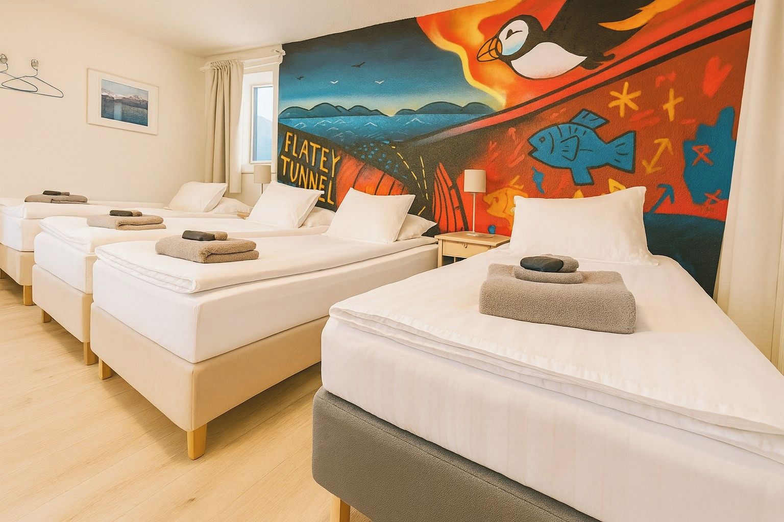 A hotel room with four single beds, each with a towel and a small pillow. The room features a large wall mural depicting a penguin and a fish, with the words 'FLATLEY TUNNEL' visible.