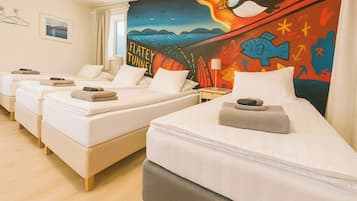 A hotel room with four single beds, each with a towel and a small pillow. The room features a large wall mural depicting a penguin and a fish, with the words 'FLATLEY TUNNEL' visible.