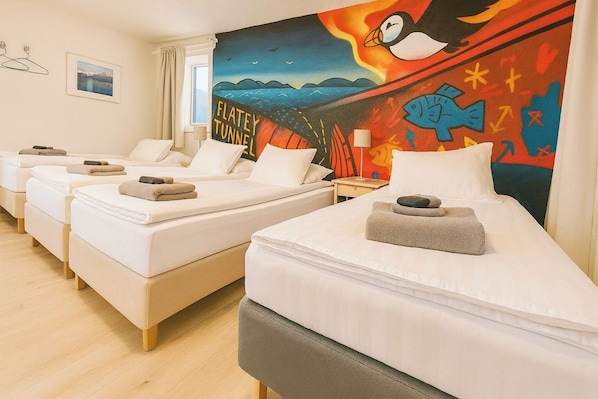A hotel room with four single beds, each with a towel and a small pillow. The room features a large wall mural depicting a penguin and a fish, with the words 'FLATLEY TUNNEL' visible. - Stykkisholmur Inn (Stykkisholmur)