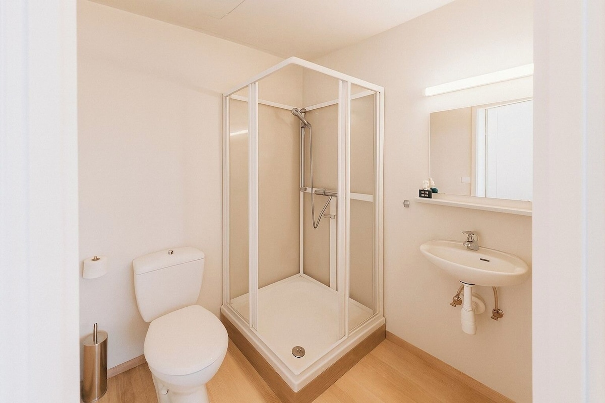 A bathroom with a glass-enclosed shower, a toilet, and a sink with a mirror above it.