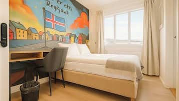 Un dormitorio con cama, escritorio, silla, ventana y un mural en la pared.