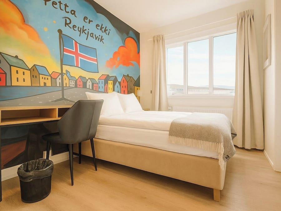 Un dormitorio con cama, escritorio, silla, ventana y un mural en la pared.