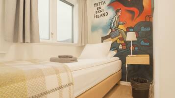 Camera da letto con un letto, una finestra, un murale, un comodino e un cestino.