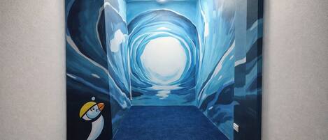 A hallway with a blue carpet and a mural of a tunnel with a penguin character.