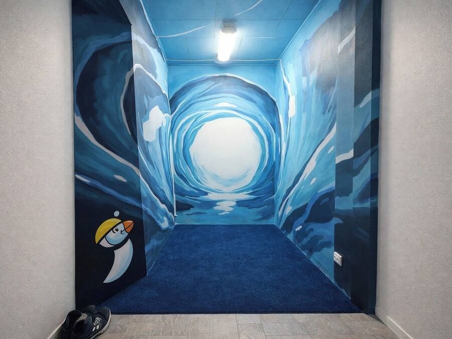 Un pasillo con alfombra azul y un mural de un túnel con un personaje de pingüino.