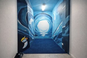 A hallway with a blue carpet and a mural of a tunnel with a penguin character. - Stykkisholmur Inn (Stykkisholmur)