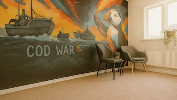 Una habitación con un mural que representa un barco y el texto 'COD WAR', una silla y un radiador.