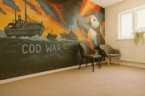A room with a wall mural depicting a ship and the text 'COD WAR,' a chair, and a radiator. - Stykkisholmur Inn (Stykkisholmur)
